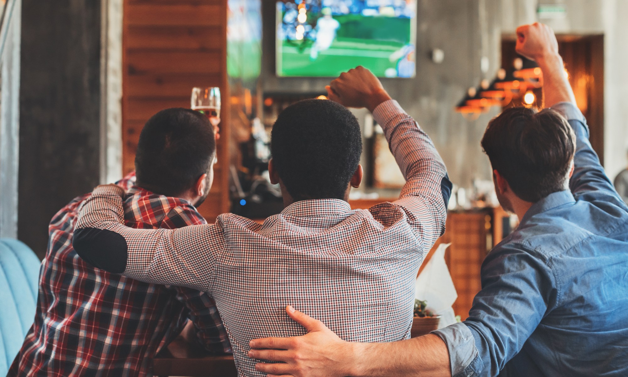 Three men seated at a bar, intently watching a football game on the television screen in front of them.